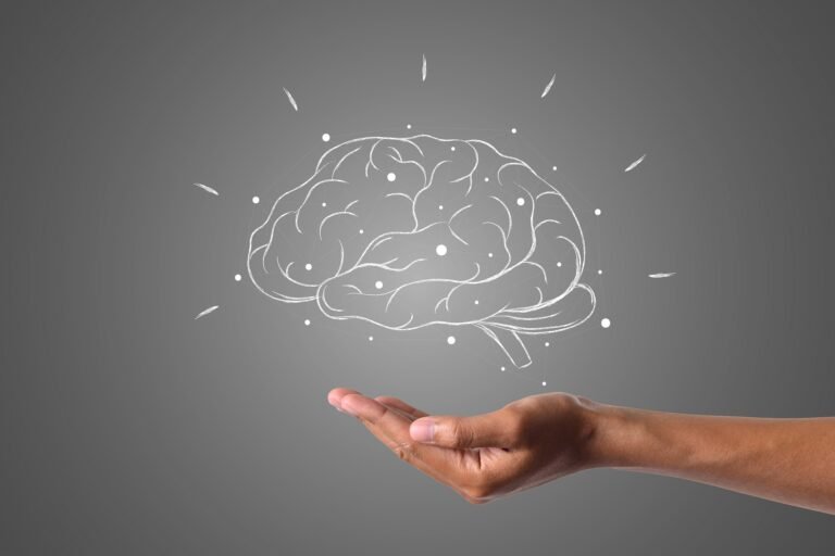 A human hand gently holding an illustrated brain made of white lines and nodes, symbolizing mental health, cognitive science, or brain support, on a dark gray background.