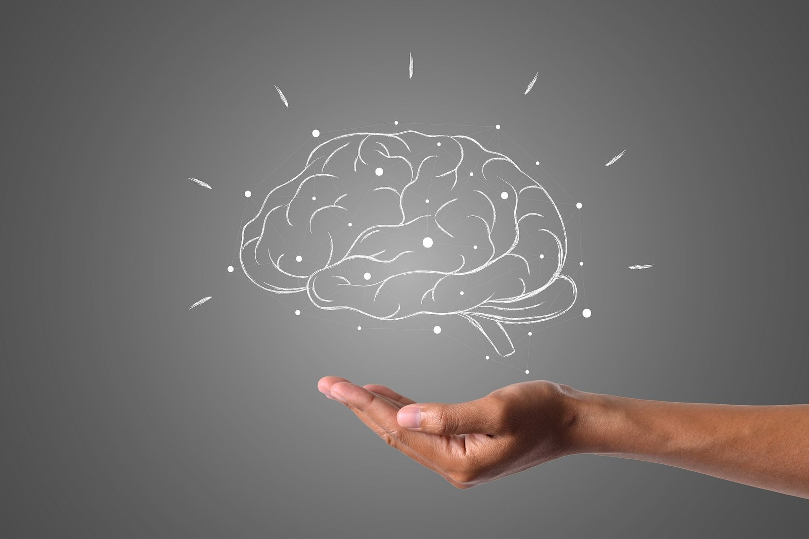 A human hand gently holding an illustrated brain made of white lines and nodes, symbolizing mental health, cognitive science, or brain support, on a dark gray background.