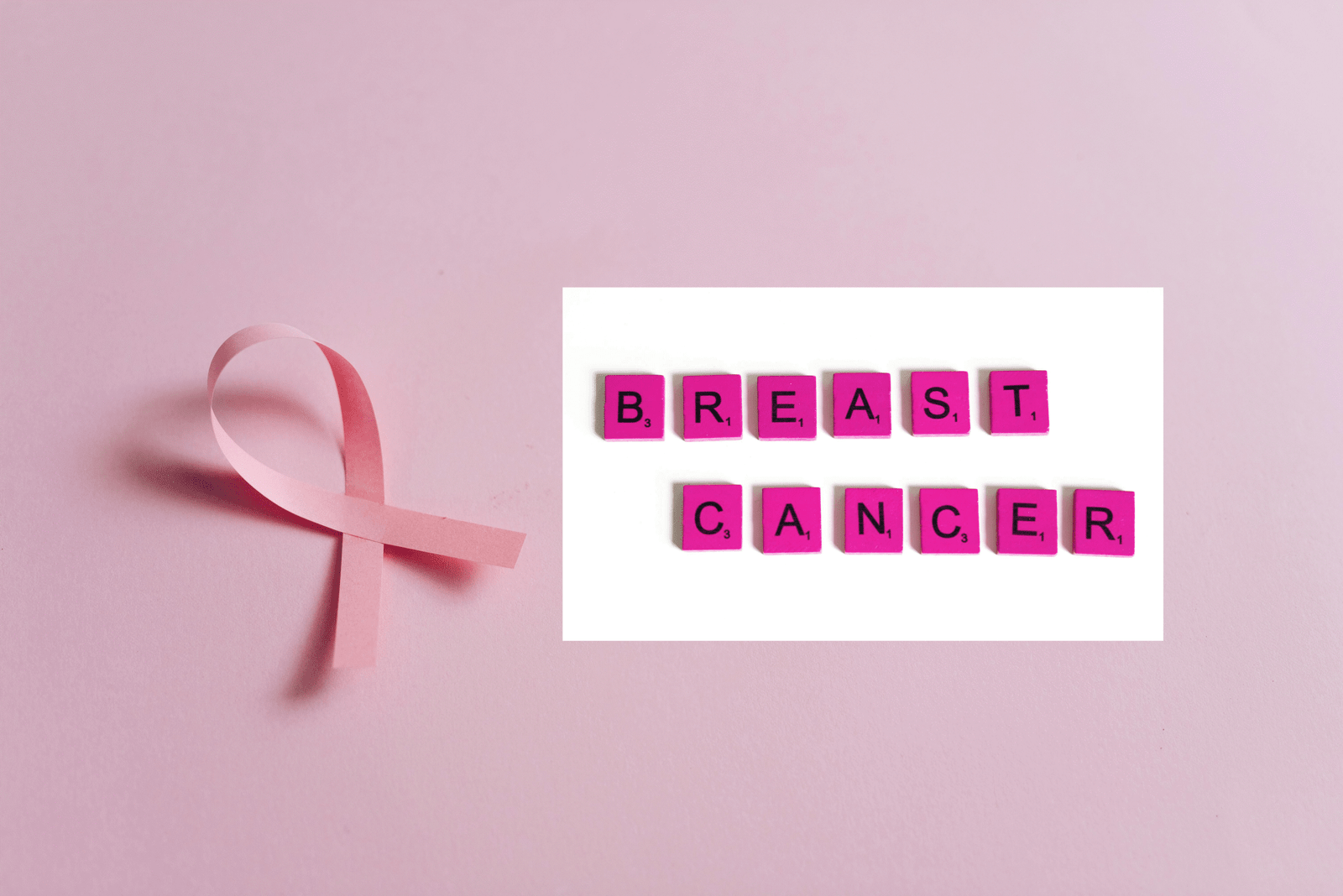 Pink Ribbon on Pink Surface with Scrabble Letter Tiles on White Background.