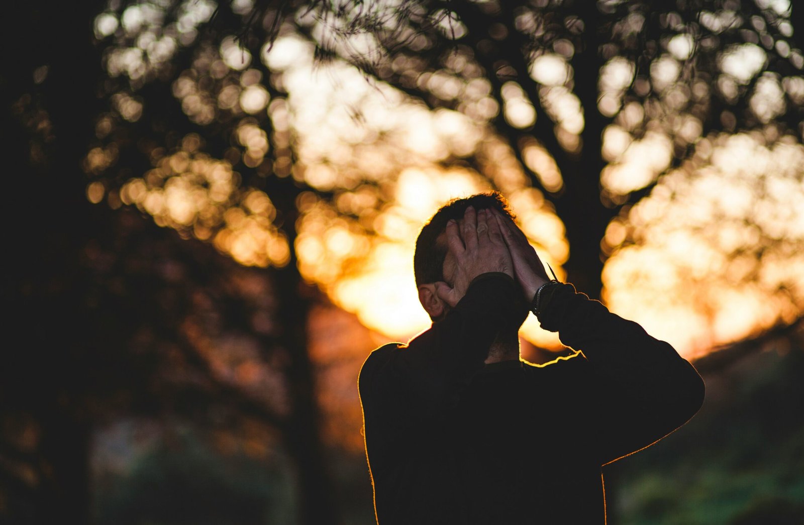Men standing, hand on his face and sunset in the background.