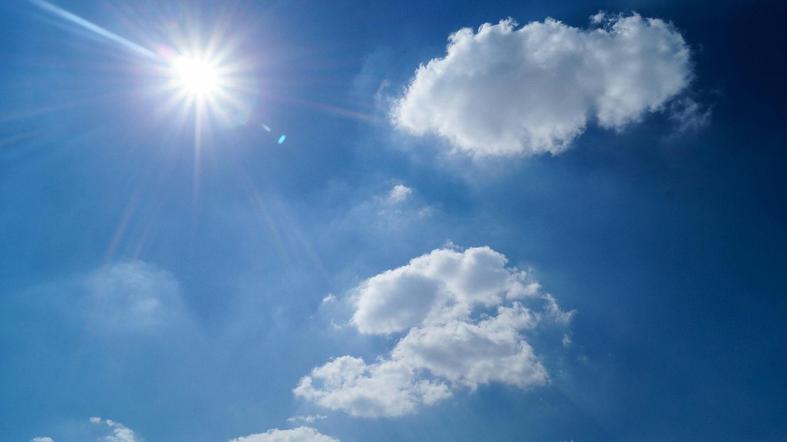 Vibrant blue sky with fluffy clouds and bright sun. 