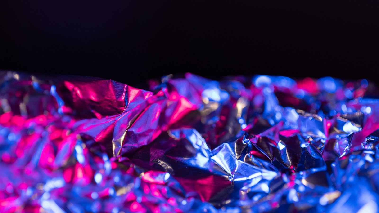 Close-up of crumpled aluminum foil with vibrant pink and blue neon lighting and blurred background.