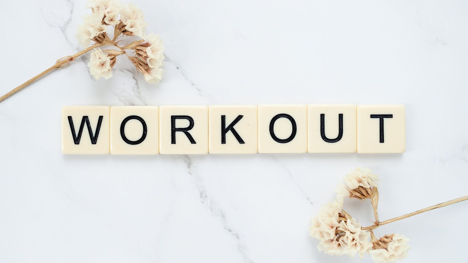 Letter tiles spelling Workout on marble with dried flowers, conveying fitness motivation.