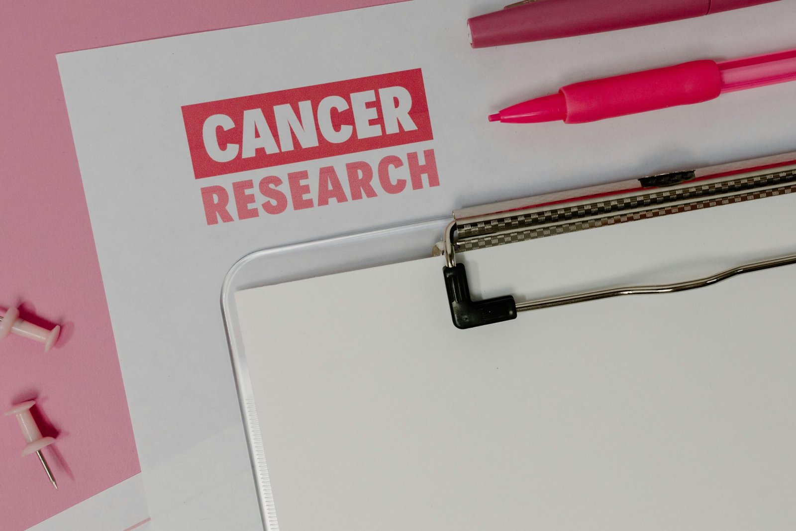 Flat lay of cancer research materials on a pink background highlighting awareness.