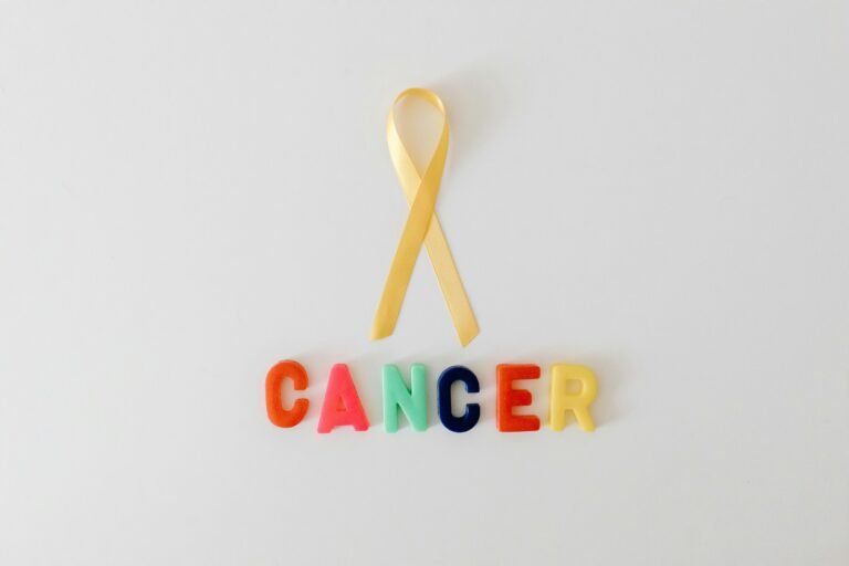 Yellow cancer awareness ribbon with colorful letters spelling 'cancer' on white background.