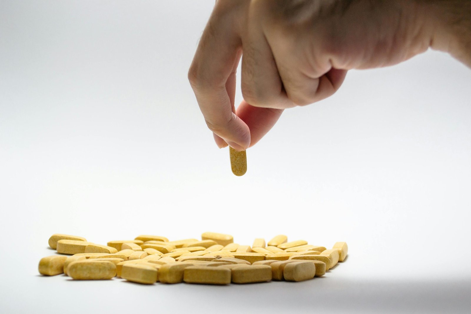 Close-up of a hand picking a supplement from a pile of tablets on a white surface.