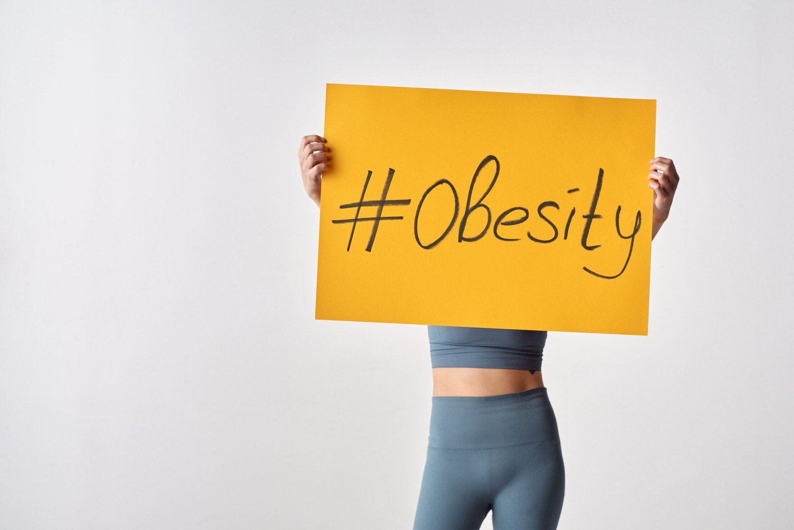 Individual holding yellow sign with hashtag 'Obesity'. Awareness concept.